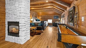 Un acogedor interior de cabaña de madera con chimenea de piedra, vigas de techo de madera, un sofá y una mesa de billar.
