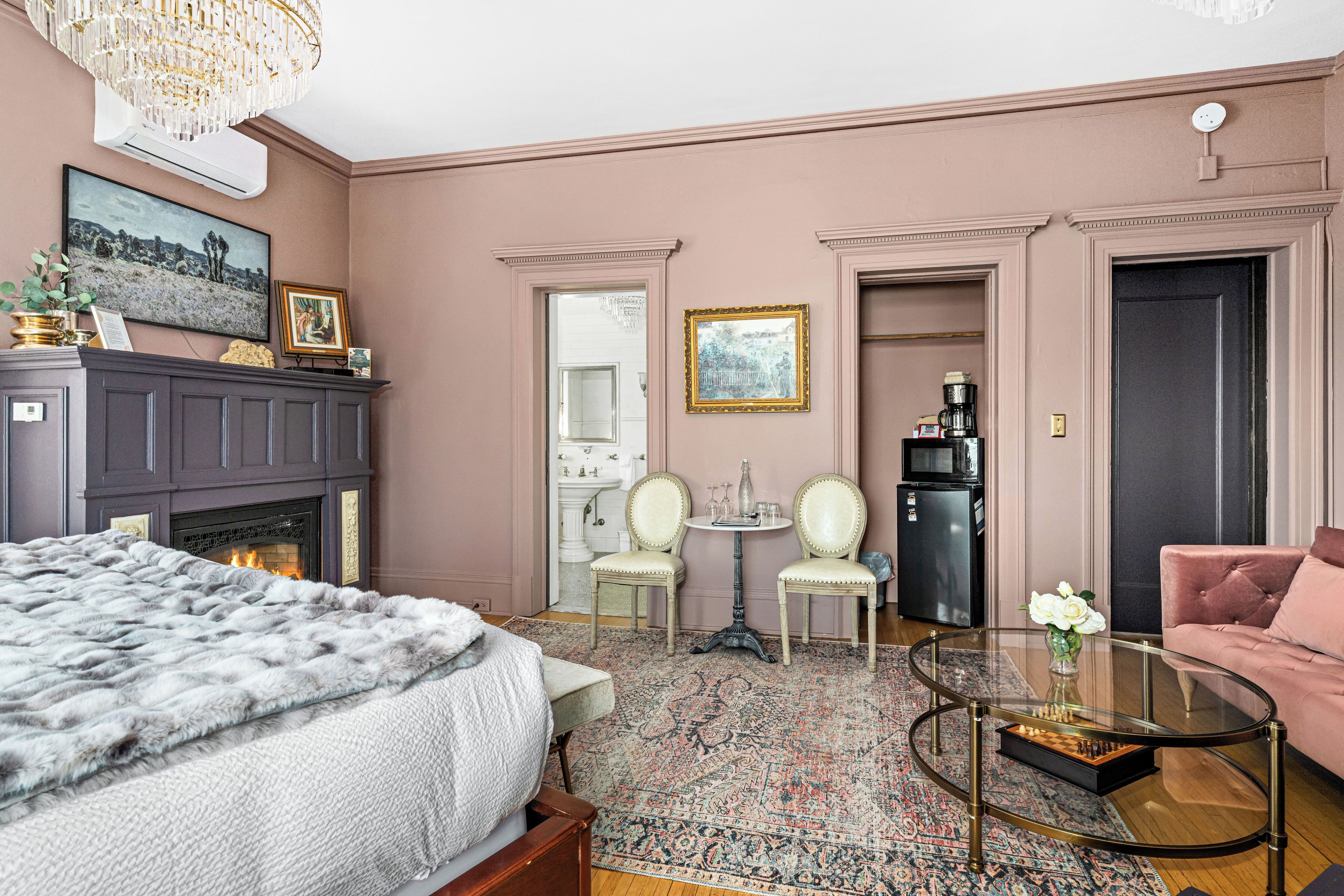 A room with a fireplace, a bed, a round coffee table, and a pink sofa.