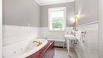 A bathroom with a large bathtub, a sink, and a window.