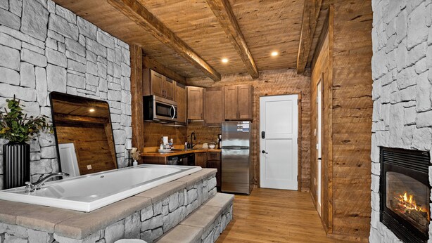 Una cocina rústica con paredes de piedra, vigas de madera, un lavamanos grande, un microondas, un refrigerador y una chimenea.