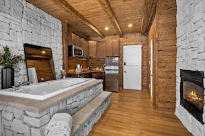 A rustic kitchen with stone walls, wooden beams, a large sink, a microwave, a refrigerator, and a fireplace.