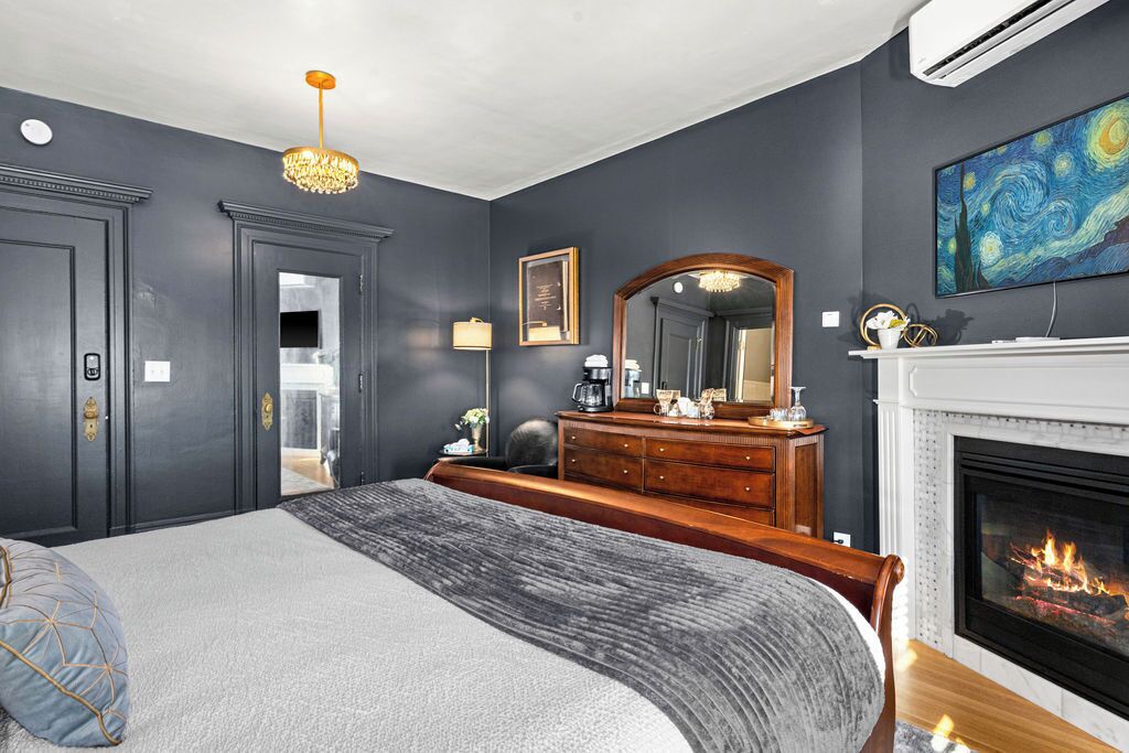 Quarto com cama grande, cômoda, espelho, lareira e um quadro na parede.