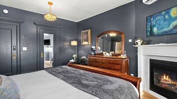 Quarto com cama grande, cômoda, espelho, lareira e um quadro na parede.