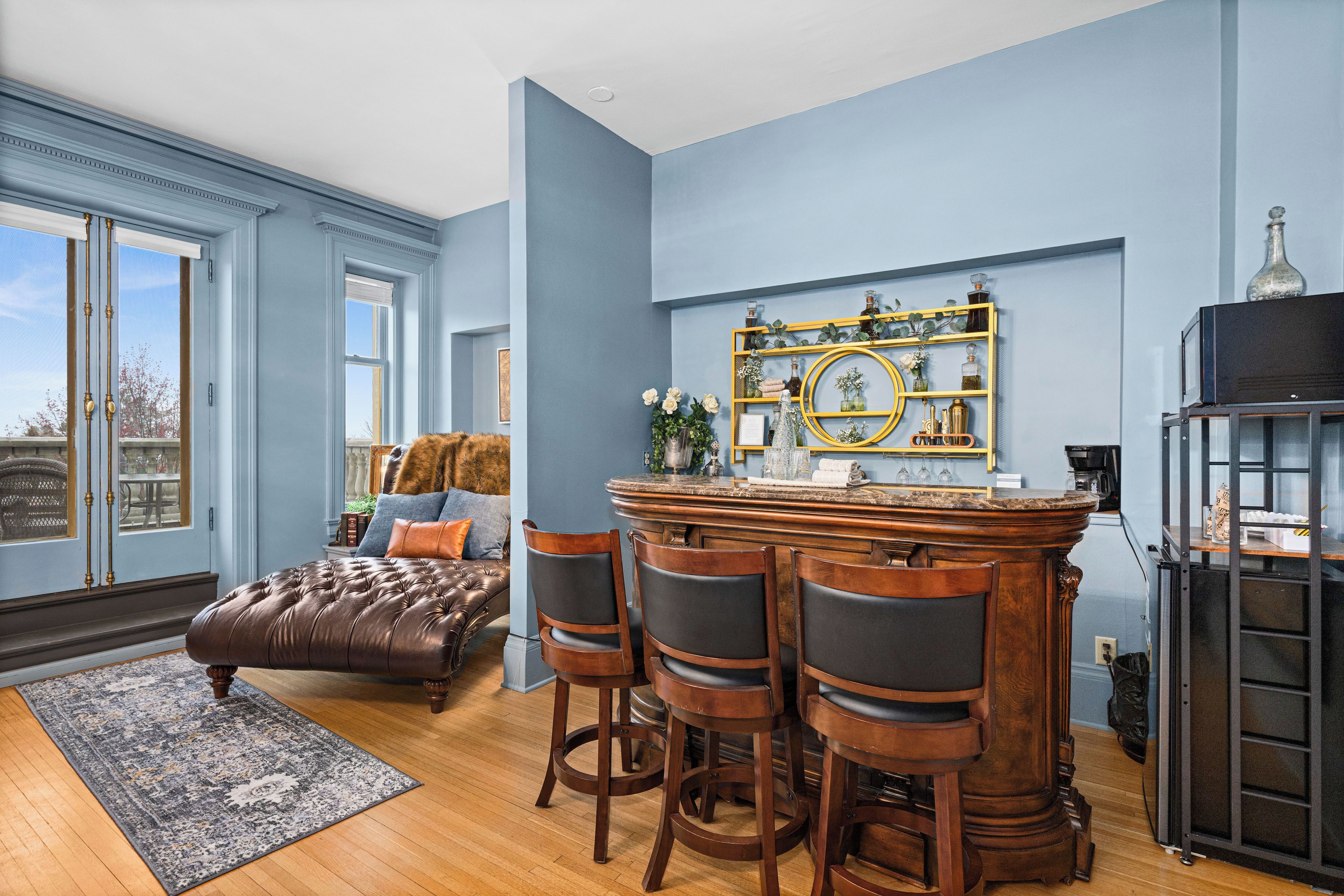 Une pièce comprenant un coin bar, une grande fenêtre et un espace salon avec un canapé et des fauteuils.