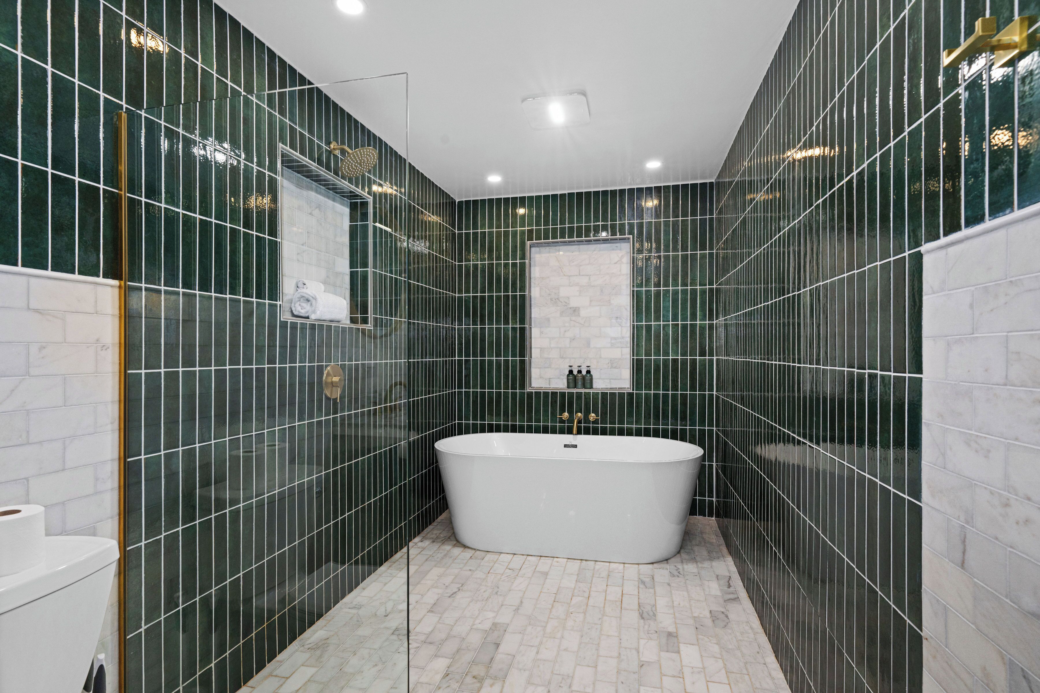 Un baño moderno con una bañera independiente, paredes de azulejos verdes y un suelo de mármol blanco.
