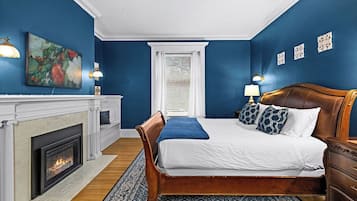 A bedroom with a fireplace, a large bed with a headboard, a blue accent wall, and a patterned rug.
