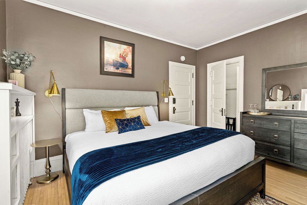 A bedroom with a large bed, a dresser, a nightstand, and a painting on the wall.