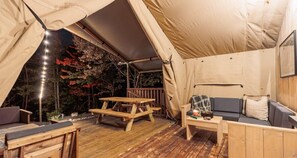 Un espacio al aire libre con carpas, una mesa de madera y bancos, un sofá y una mesita con un objeto decorativo.