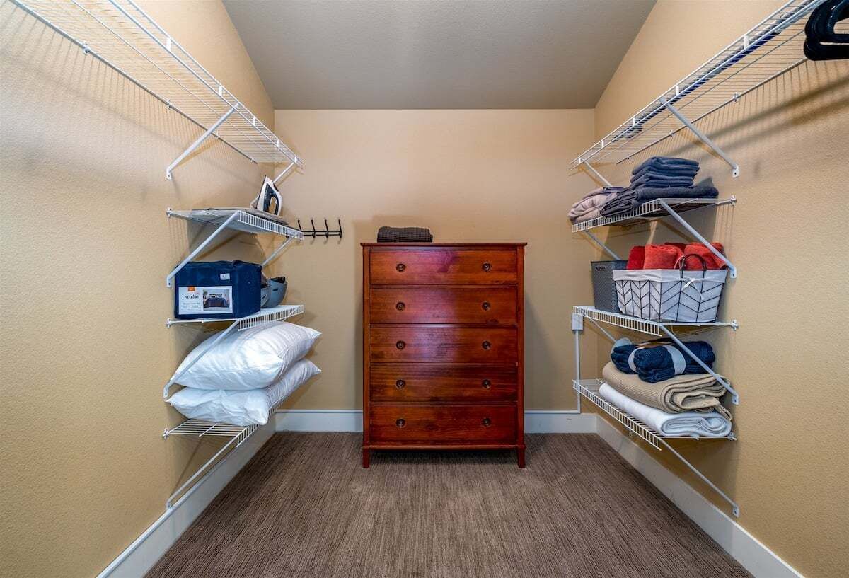 A small, narrow hallway with beige walls, a wooden dresser, and metal shelving units on either side.