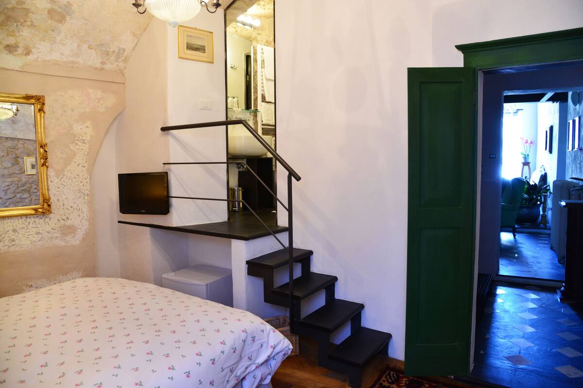 Ein Schlafzimmer mit einem Bett, einer Treppe, einem Spiegel und einer grünen Tür zu einem weiteren Raum.