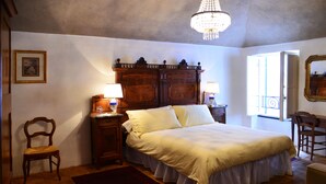 A bedroom with a large bed, wooden headboard, two bedside tables with lamps, a wooden chair, a red rug, and a chandelier. - La Terrazza di Vico Olivi B&B  (Ventimiglia)
