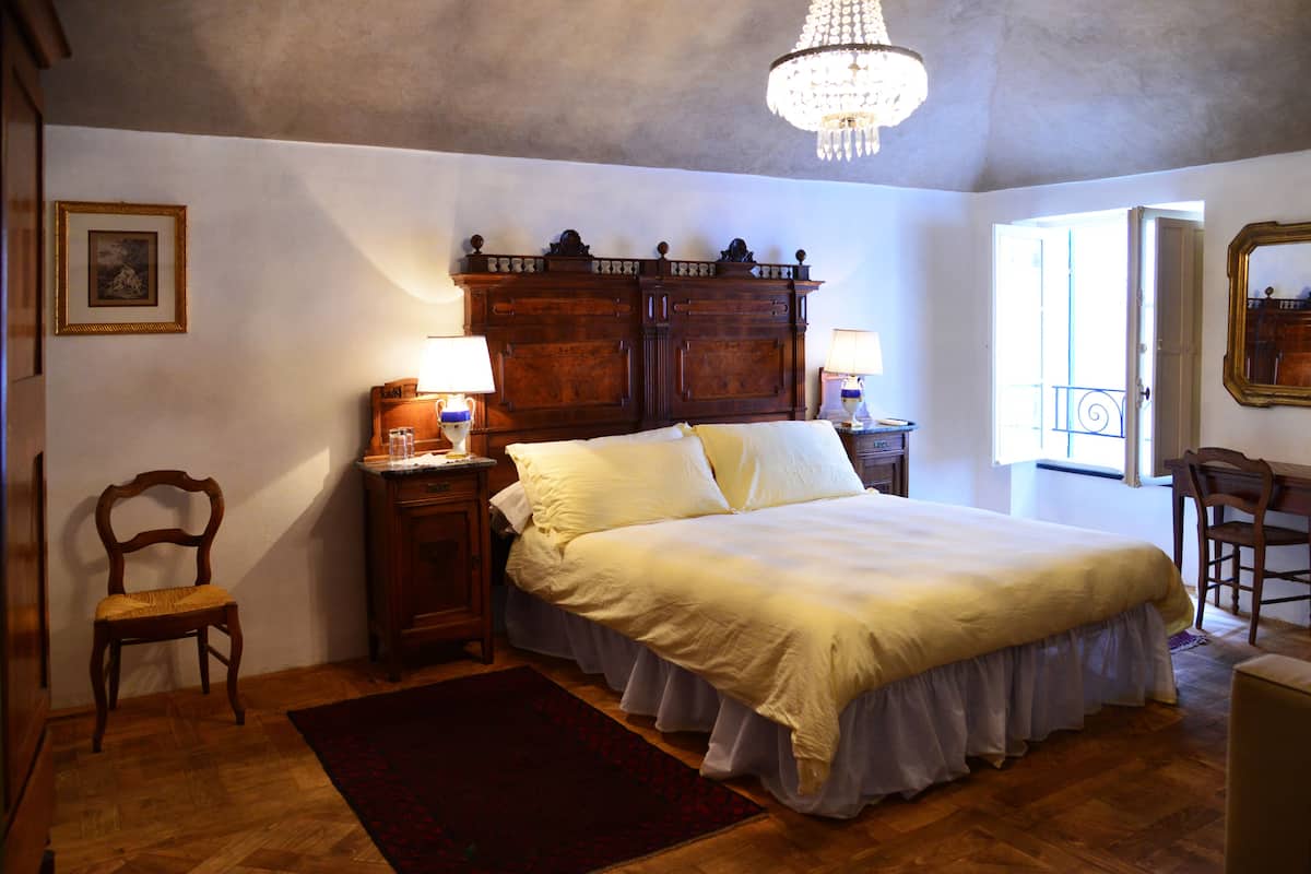 Ein Schlafzimmer mit einem großen Bett, einem Holzkopfteil, zwei Nachttischen mit Lampen, einem Holzstuhl, einem roten Teppich und einer Chandelier.