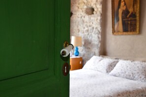 A green door with a keyhole and a lock. In the background, there is a bed with white bedding and a lamp on a nightstand. - La Terrazza di Vico Olivi B&B  (Ventimiglia)