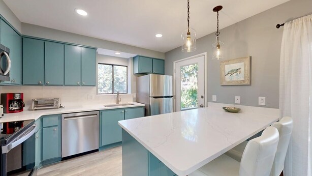 A modern kitchen with teal cabinets, a white marble island, stainless steel appliances, and pendant lighting. - Wonderfully Decorated Two Bedroom Water Oak Villa! (Hilton Head)