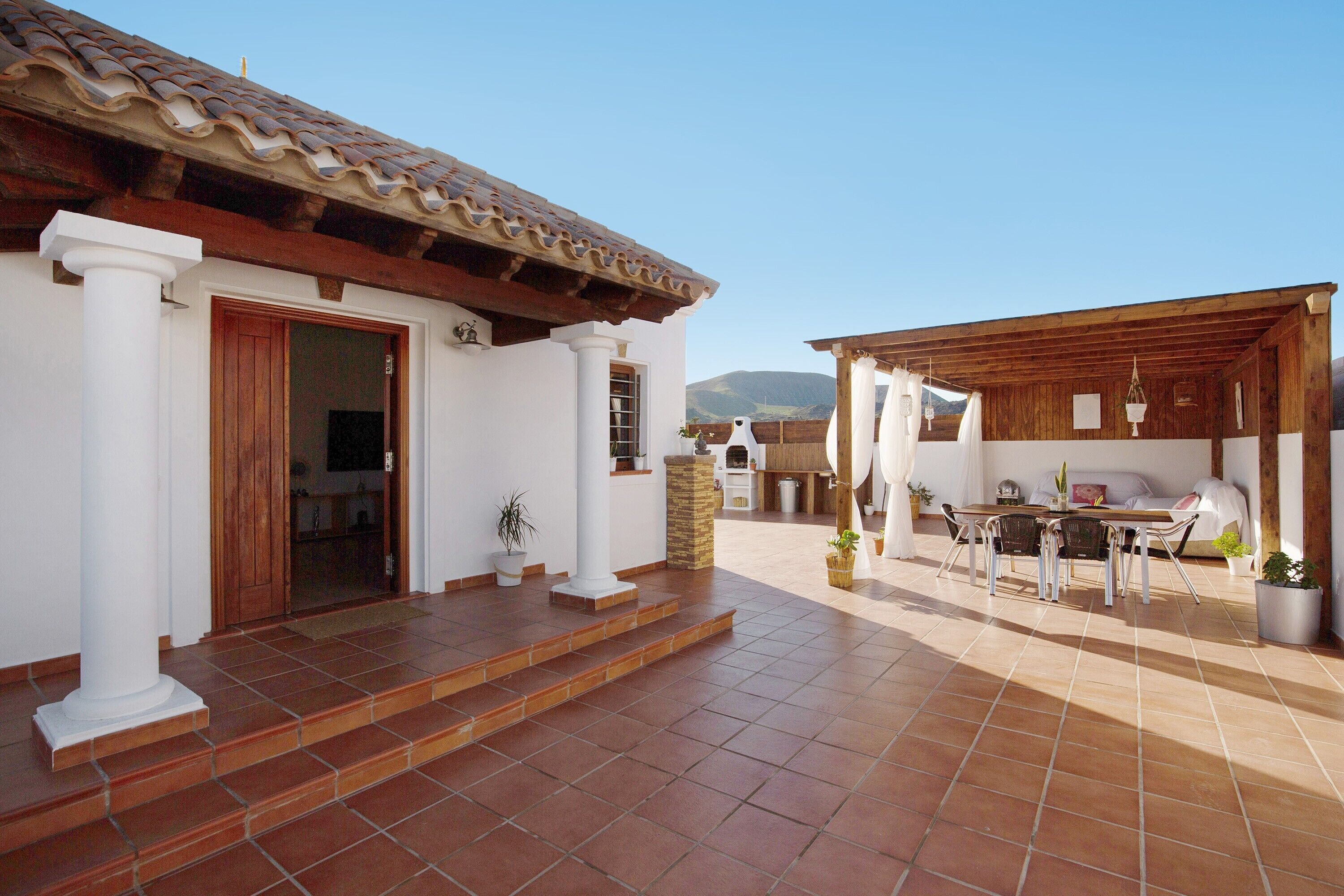 Un patio con una mesa, sillas, un pilar blanco y una puerta.