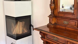 A room with a white wood-burning stove, a wooden cabinet with ornate carvings, and a mirror reflecting a kitchen area. - Apartment "Vorderschöneck 2" with Mountain View, Shared Garden & Wi-Fi (Longostagno)