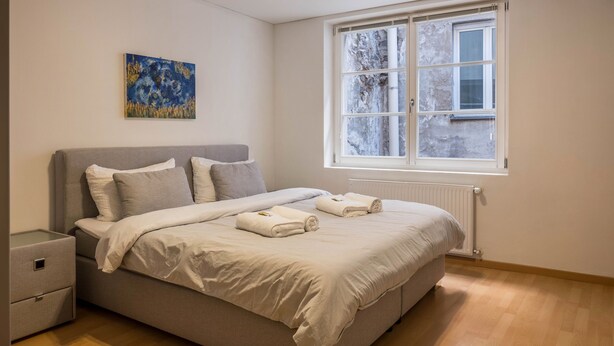Ein Schlafzimmer mit einem Bett, einem Nachttisch, einem Fenster und einem Bild an der Wand.