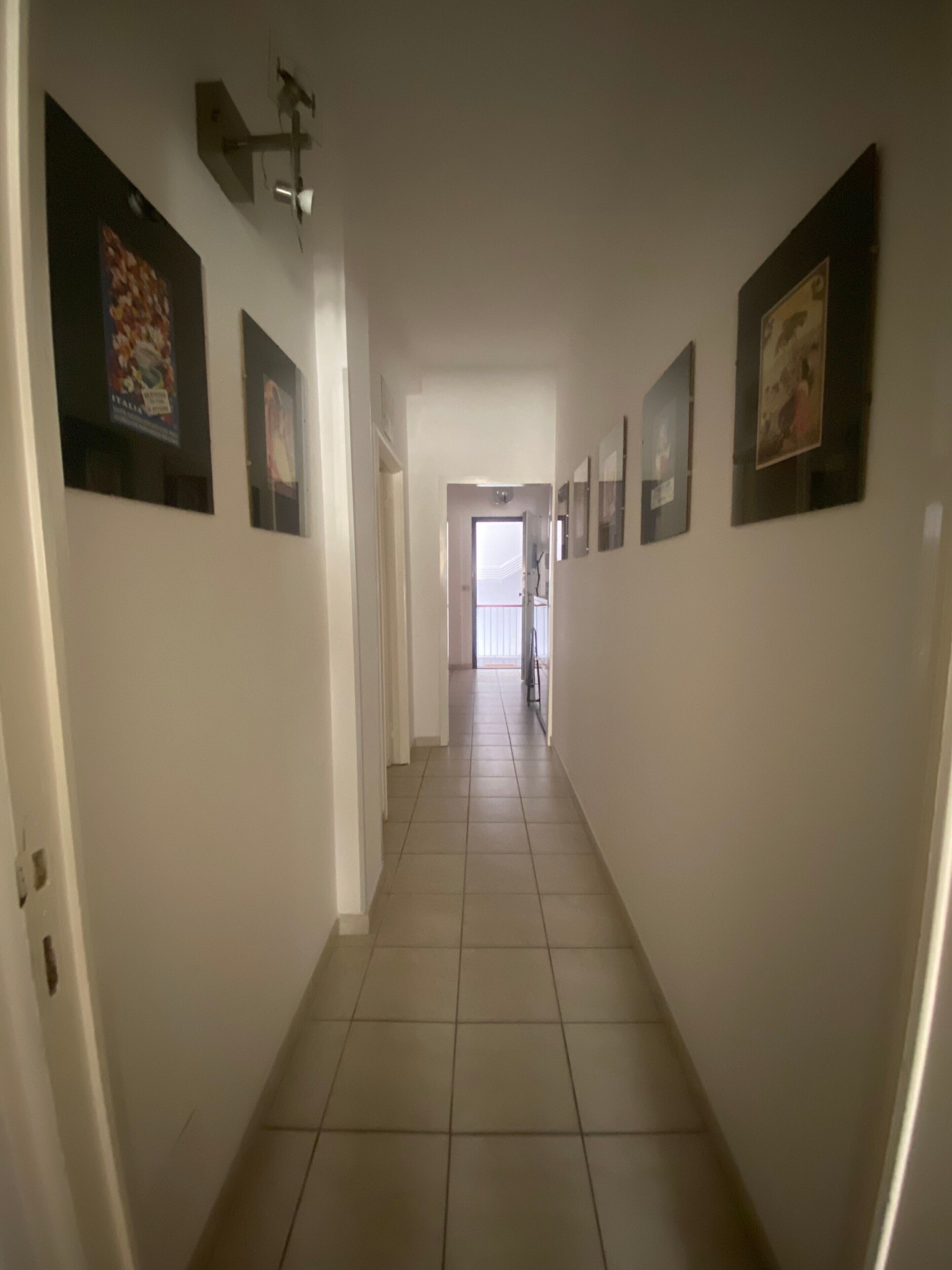 Un corridoio con pavimento piastrellato e pareti decorate con quadri incorniciati.
