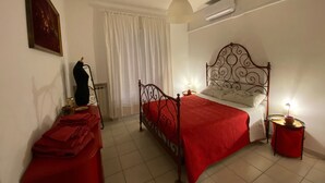Ein Schlafzimmer mit einem Bett, einem Nachttisch, einer Lampe, einer Hängelampe und einem Fenster mit Vorhängen.