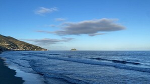 Eine Küstenlandschaft mit Strand, Meereswellen, einer entfernten Insel und einem gebirgigen Gebiet mit Gebäuden.