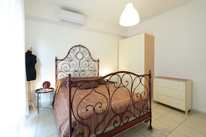 Une chambre à coucher avec un lit en métal, une table de chevet, une commode et un mannequin.