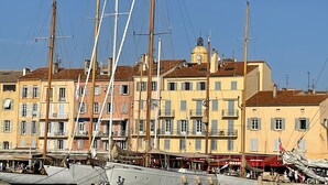 Un puerto deportivo con veleros amarrados, edificios con balcones y una torre del reloj.