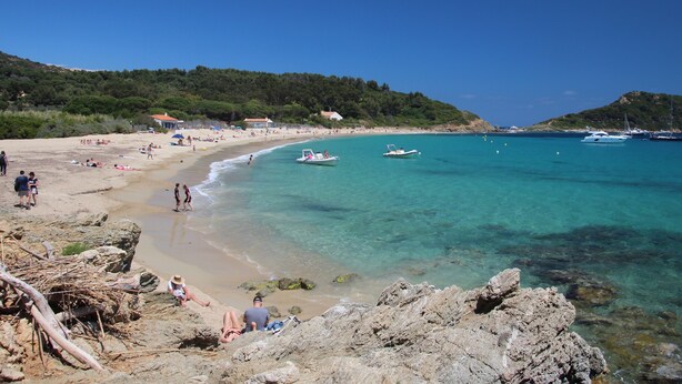 Una playa con agua turquesa cristalina, costa rocosa y barcos.