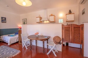 A room with a bed, a table with chairs, a hat, a lamp, and a shelf with decorative items. - Studio "Le Val de Pons Ramatuelle", with private terrace & Wi-Fi (Ramatuelle)