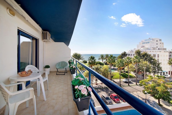 Un balcon avec une table et des chaises, des plantes en pot et une vue sur la mer et les bâtiments.