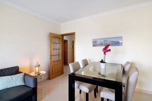 Un coin repas comprenant une table en verre, des chaises, une petite table d’appoint avec une lampe, et une porte donnant sur une autre pièce.