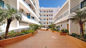 A courtyard with a brick floor, palm trees, and a white building with balconies.
