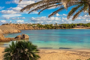 A coastal landscape with clear turquoise waters, rocky cliffs, and a sandy beach.
