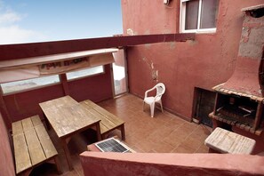 Un balcón con mobiliario de madera, una silla de plástico blanco y un horno de ladrillo.