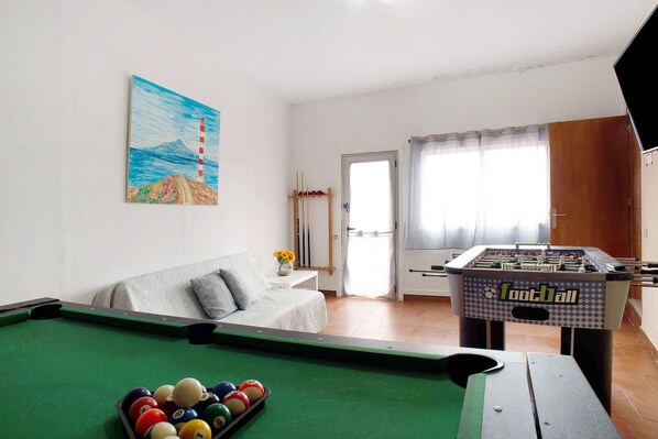 Una habitación con mesa de billar, sofá, mesa de fútbolín y un cuadro en la pared.