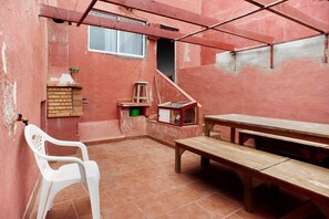 Un patio con un banco de madera, una silla de plástico blanco y un muro de ladrillo.