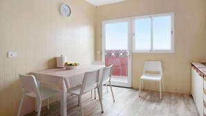 A dining area with a table and chairs, a clock on the wall, and a sliding glass door leading to a balcony.