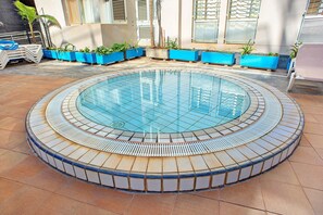 A circular pool with a tiled edge, surrounded by blue planters with plants, and a tiled floor.