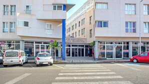 Um edifício de vários andares com design arquitetônico moderno, destacando uma entrada imponente com portas de vidro, diversas janelas e um pilar estrutural azul.