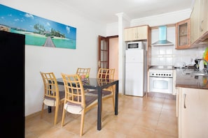 Un comedor con una mesa y sillas, una cocina con estufa y refrigerador, y un cuadro de una playa en la pared.