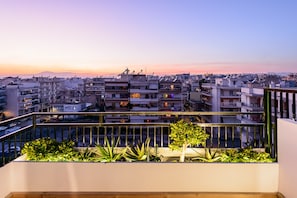 A balcony with plants and a view of a cityscape at sunset.