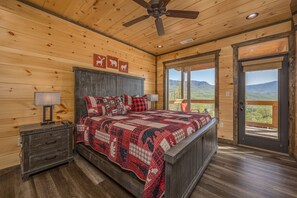A wooden cabin bedroom with a bed, nightstands, and a view of mountains through the door. - Free Attractions! Private Indoor Heated Pool, Hot Tub, Great Views, Games (Gatlinburg)