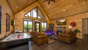 Un cuarto acogedor con mesa de billar, dos sofás, chimenea y ventanas amplias que ofrecen vistas al exterior.