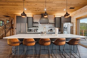 A modern kitchen with a large island, bar stools, and pendant lighting. - Panoramic Views, Hot Tub, Arcade Games, & Free Attraction Passes (Sevierville)