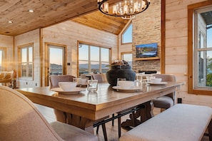 A wooden interior with a dining table set for four, a stone fireplace, and a television mounted on a stone wall. - Panoramic Views, Hot Tub, Arcade Games, & Free Attraction Passes (Sevierville)