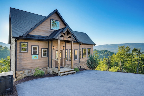 A wooden cabin with a porch, a mountain view, and a clear sky.