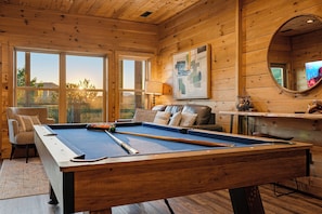 A pool table in a room with wooden walls and large windows.