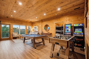 A wooden-floored room with a pool table, foosball table, and arcade games.