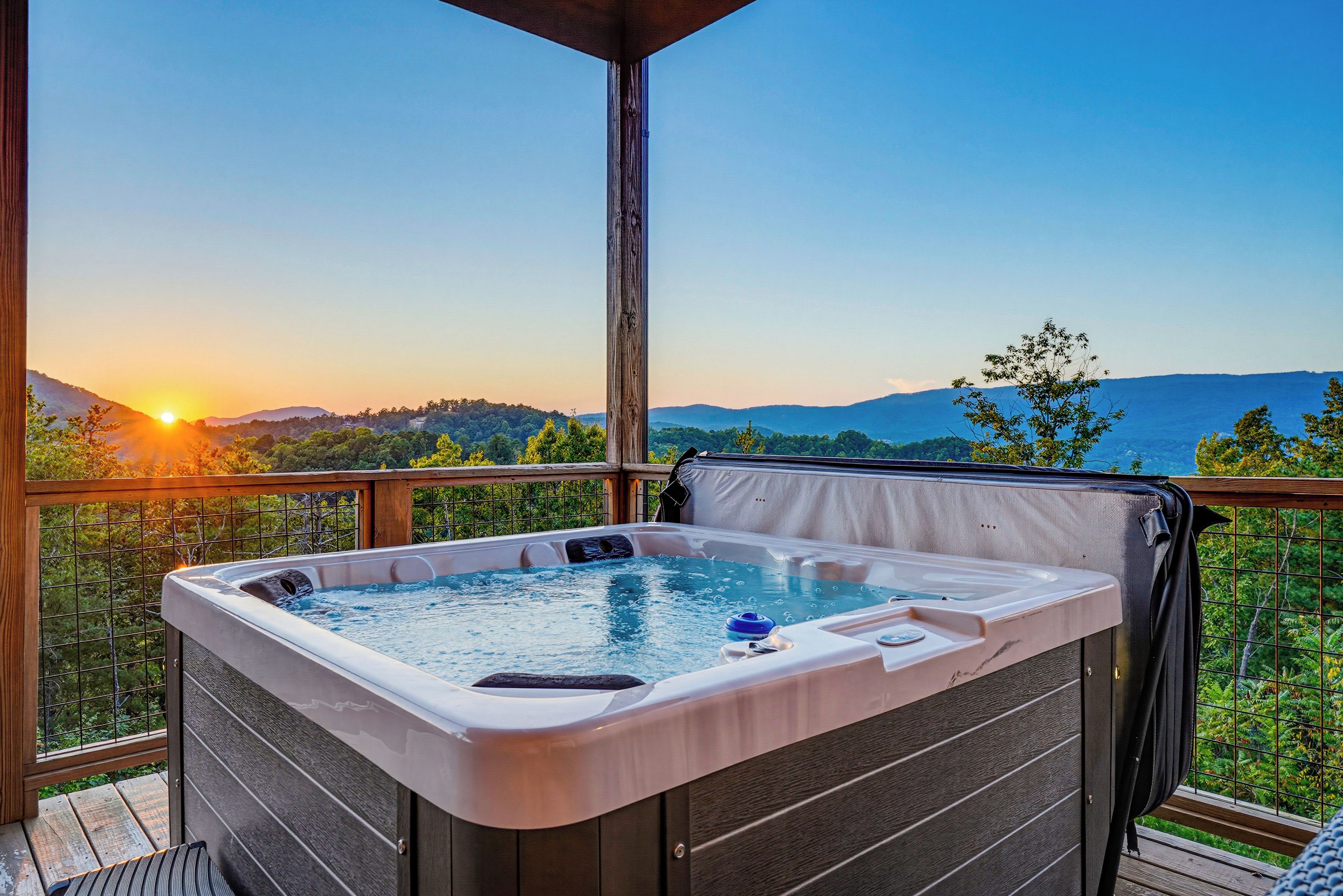A hot tub on a balcony with a scenic view of mountains and a sunset.