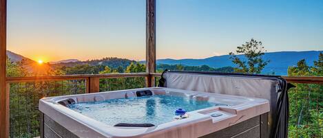 A hot tub on a balcony with a scenic view of mountains and a sunset.