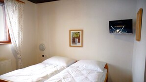 A bedroom with two single beds, a bedside table, a wall-mounted TV, and a window with curtains. - Chata Ještědka (Svetla pod Jestedem)